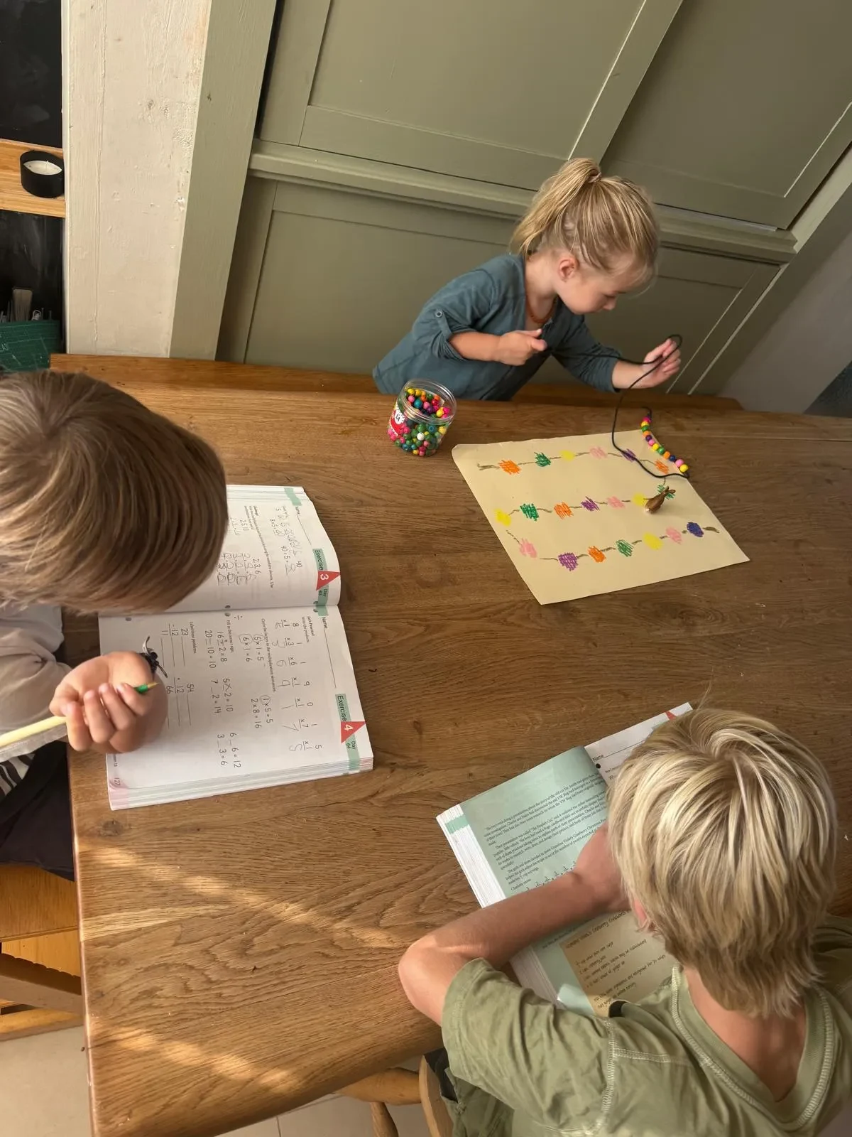 children doing different home school subjects at the same time on the kitchen table